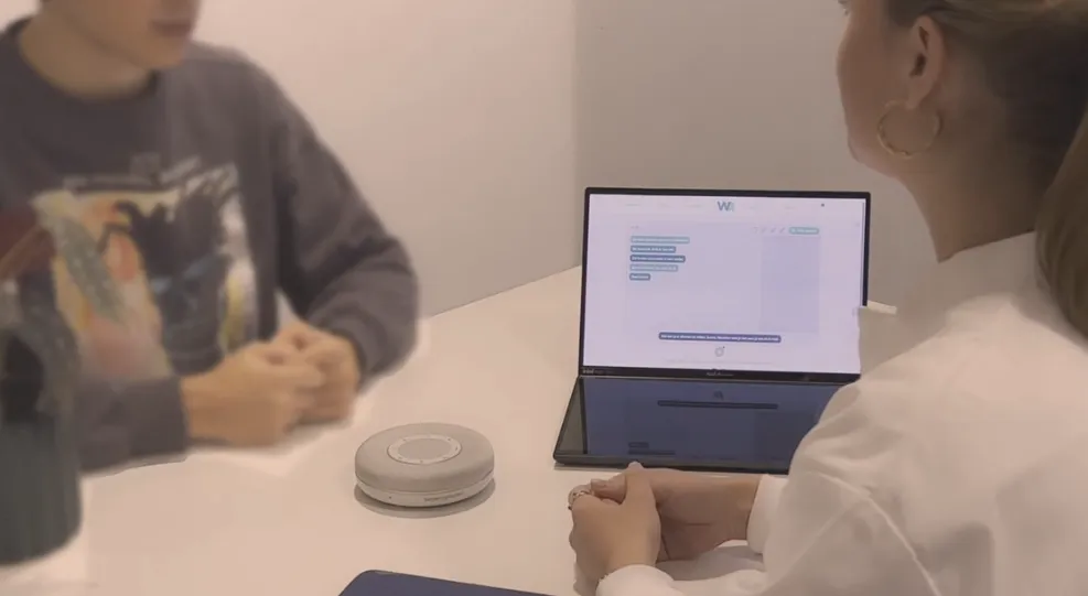 Zorgverlener in gesprek met een cliënt, met de Wellcom-microfoon op tafel en het portaal open op de laptop